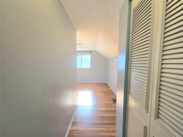 hall with hardwood / wood-style flooring, lofted ceiling, and a textured ceiling