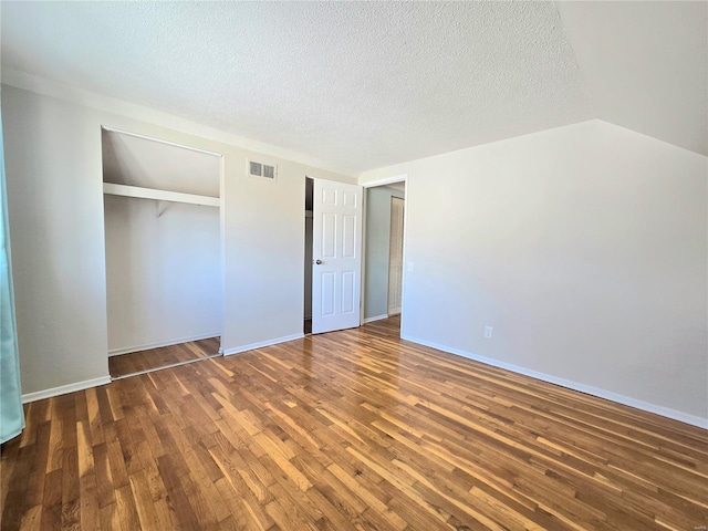 unfurnished bedroom featuring vaulted ceiling, dark wood-type flooring, a textured ceiling, and a closet