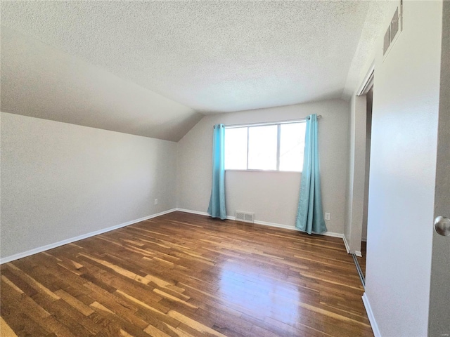 additional living space featuring dark hardwood / wood-style floors, vaulted ceiling, and a textured ceiling