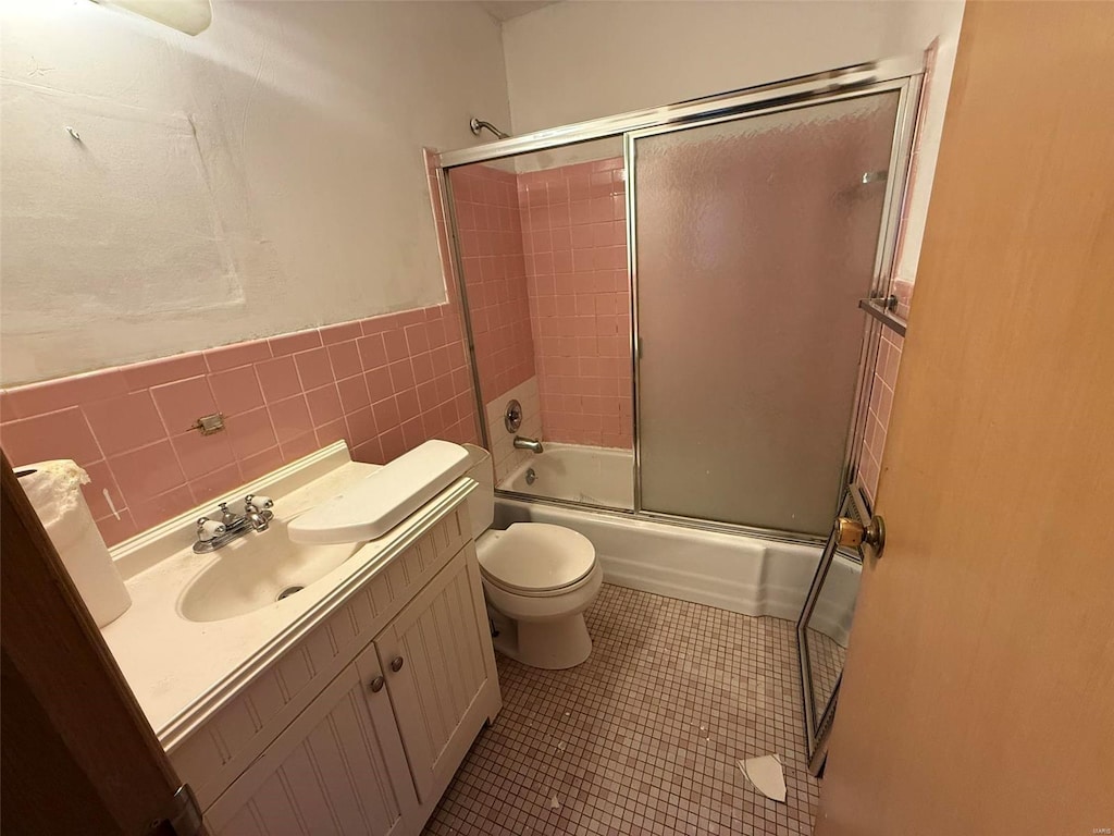 full bathroom featuring tile patterned flooring, bath / shower combo with glass door, toilet, vanity, and tile walls