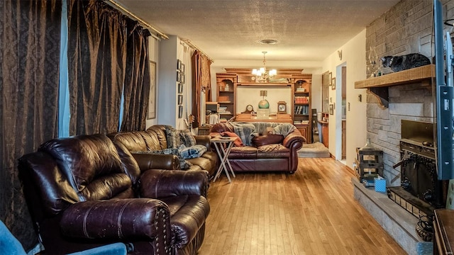 living room with a fireplace, light wood-type flooring, a textured ceiling, and a notable chandelier