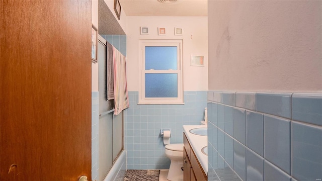 full bathroom with vanity, tile patterned floors, bath / shower combo with glass door, toilet, and tile walls