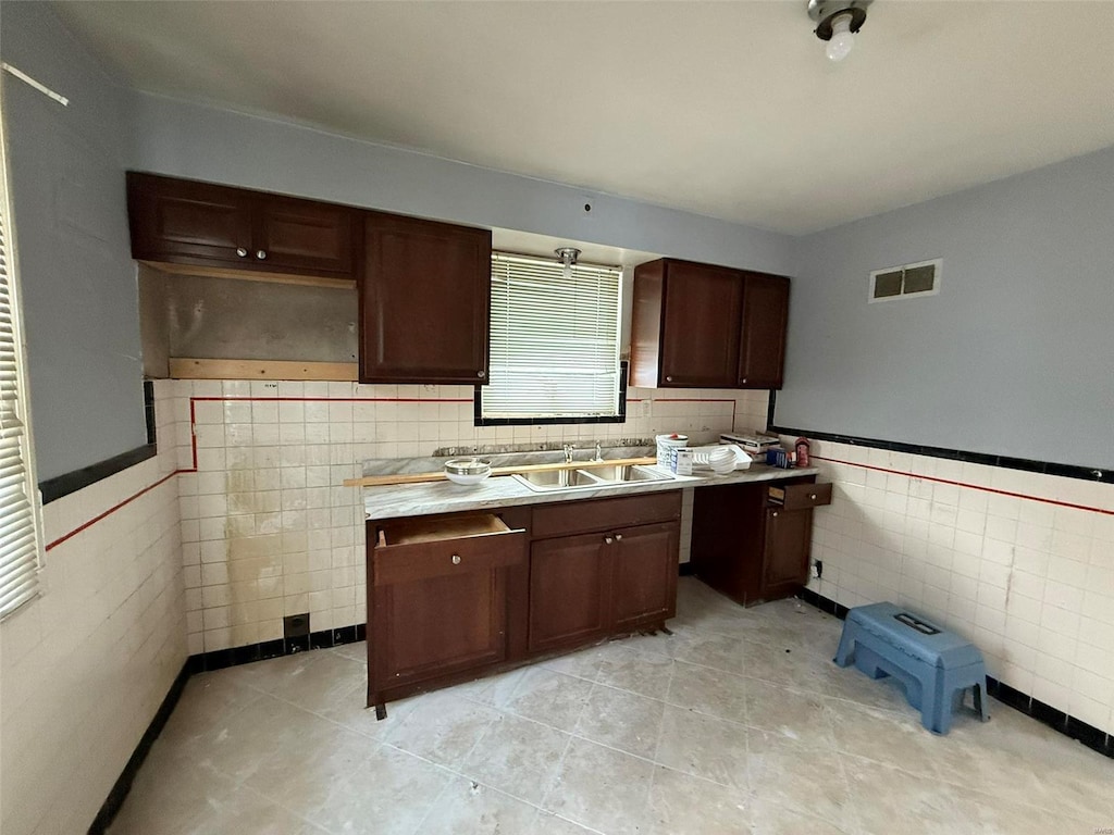 kitchen featuring dark brown cabinetry, sink, and tile walls