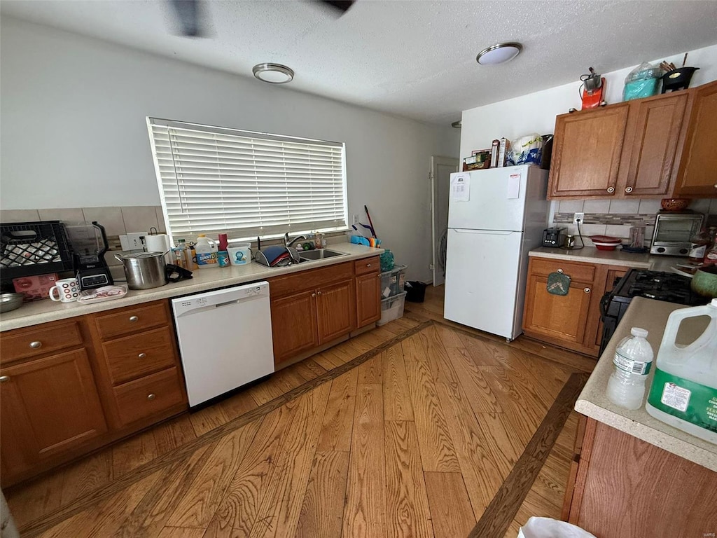 kitchen with decorative backsplash, light hardwood / wood-style floors, white appliances, and sink