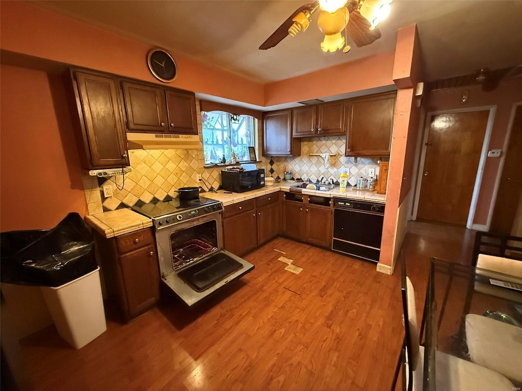 kitchen featuring black appliances, ceiling fan, decorative backsplash, tile counters, and light hardwood / wood-style floors