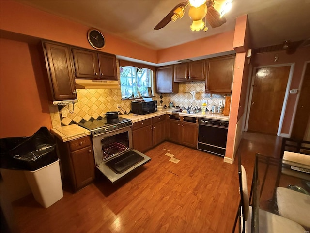 kitchen featuring black appliances, ceiling fan, decorative backsplash, tile counters, and light hardwood / wood-style floors