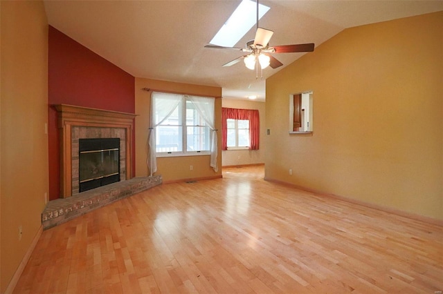 unfurnished living room with vaulted ceiling with skylight, ceiling fan, light hardwood / wood-style flooring, and a brick fireplace