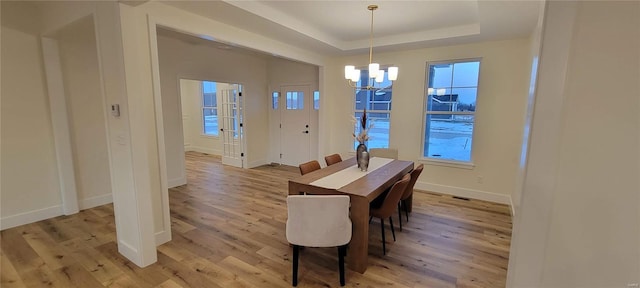 dining room featuring an inviting chandelier, a tray ceiling, and light wood-type flooring