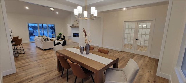 dining area featuring light hardwood / wood-style flooring, a notable chandelier, a fireplace, and french doors