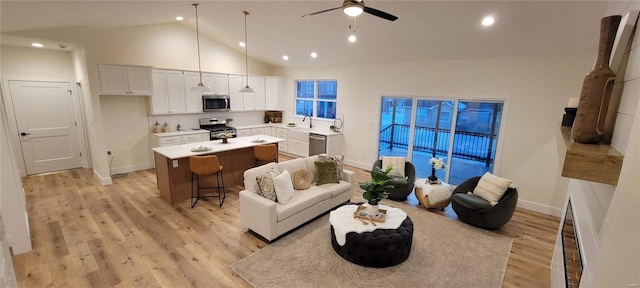 living room with vaulted ceiling, ceiling fan, and light wood-type flooring