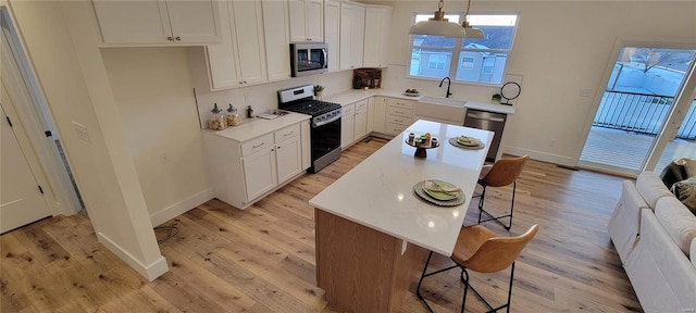 kitchen with appliances with stainless steel finishes, a center island, pendant lighting, and white cabinets