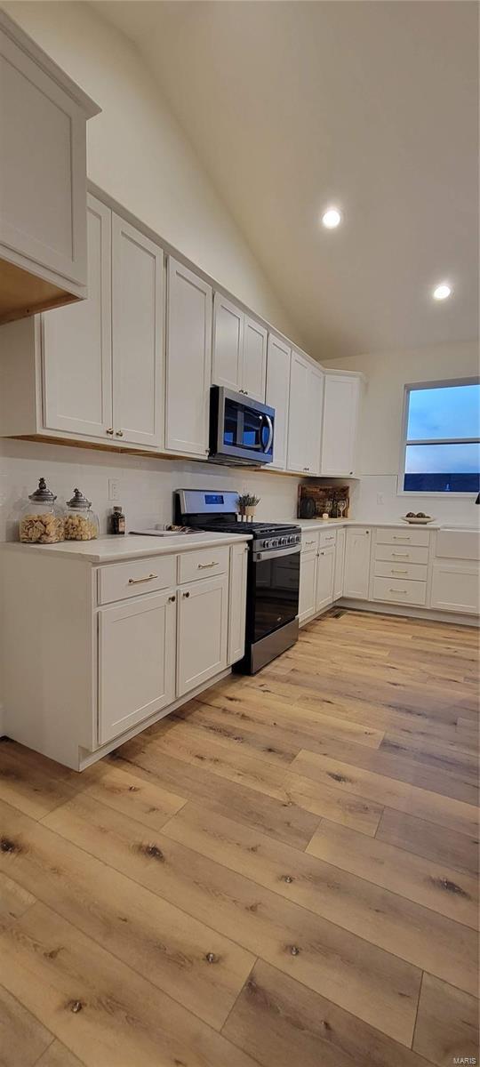 kitchen with stainless steel appliances, white cabinetry, lofted ceiling, and light wood-type flooring