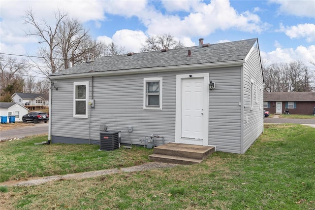 rear view of house featuring central air condition unit and a lawn