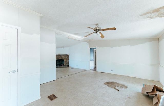 spare room featuring ceiling fan, a stone fireplace, ornamental molding, and a textured ceiling