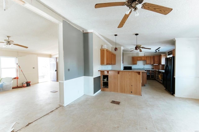 kitchen with a textured ceiling, hanging light fixtures, black fridge, kitchen peninsula, and crown molding