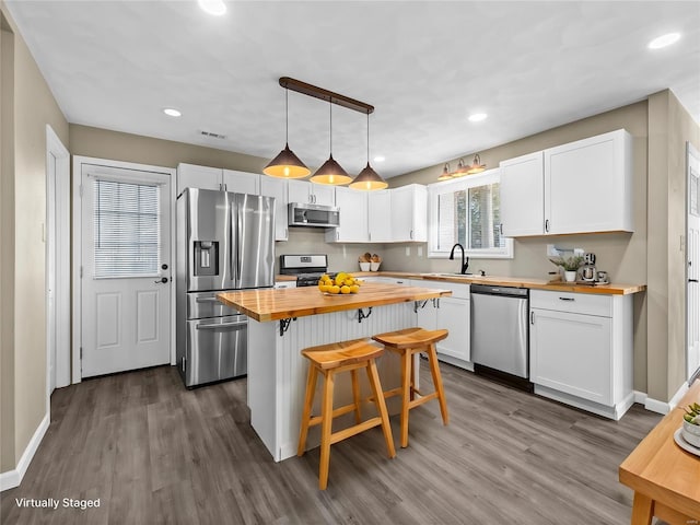 kitchen with wooden counters, a breakfast bar, hanging light fixtures, stainless steel appliances, and white cabinets