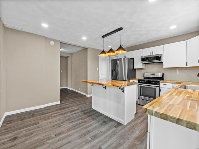 kitchen with wood counters, white cabinetry, a breakfast bar, and appliances with stainless steel finishes