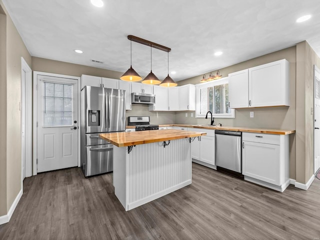 kitchen featuring appliances with stainless steel finishes, butcher block countertops, hanging light fixtures, and white cabinets