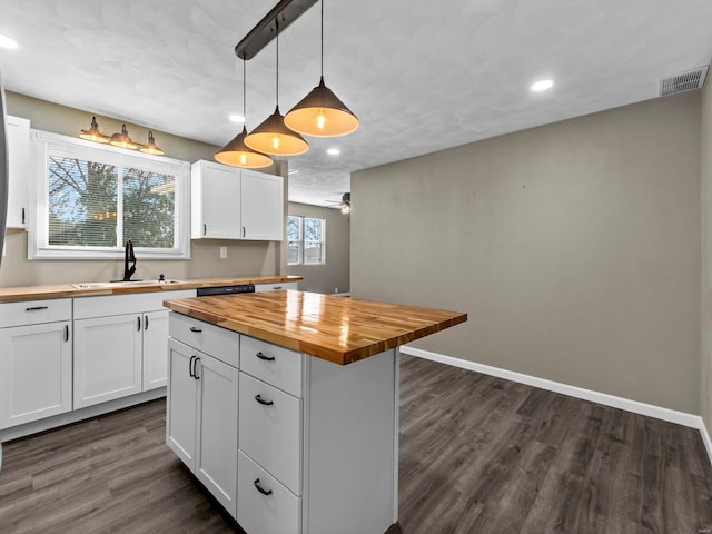 kitchen featuring butcher block countertops, decorative light fixtures, white cabinetry, sink, and a center island