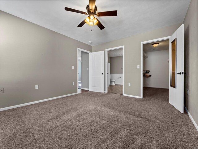 unfurnished bedroom with ensuite bathroom, a spacious closet, ceiling fan, dark carpet, and a closet