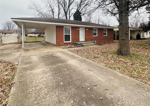 single story home featuring brick siding, concrete driveway, fence, and a carport