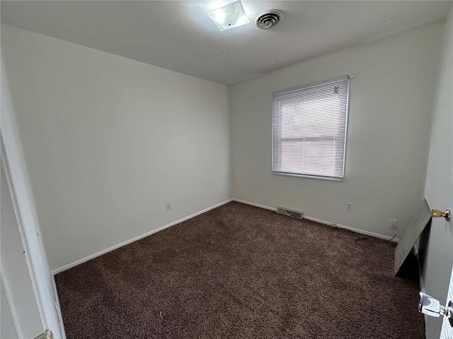 spare room featuring dark colored carpet, visible vents, and baseboards