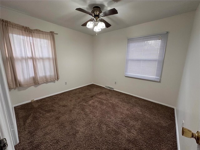 empty room featuring visible vents, dark carpet, baseboards, and ceiling fan