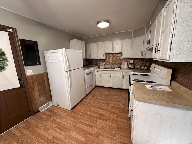 kitchen featuring light wood finished floors, a sink, white appliances, wainscoting, and light countertops