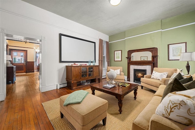 living room with hardwood / wood-style flooring, a baseboard heating unit, a textured ceiling, and a tiled fireplace