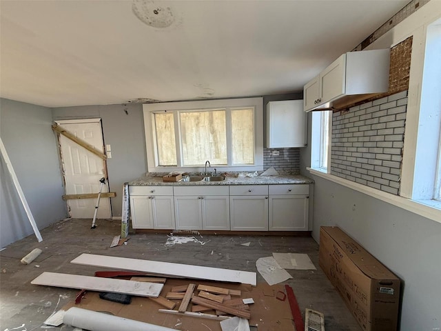 kitchen with backsplash, light stone counters, white cabinetry, and sink