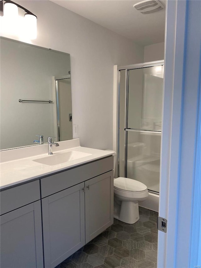 bathroom featuring tile patterned flooring, vanity, toilet, and a shower with shower door