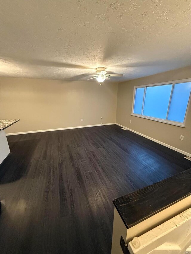 unfurnished room featuring baseboards, dark wood-type flooring, ceiling fan, and a textured ceiling