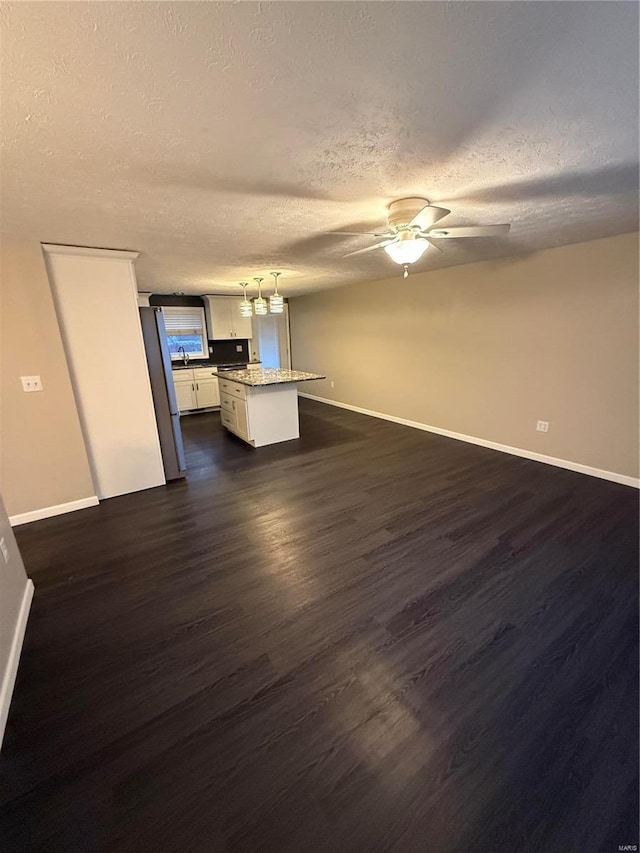 unfurnished living room featuring dark wood finished floors, ceiling fan, a textured ceiling, and baseboards