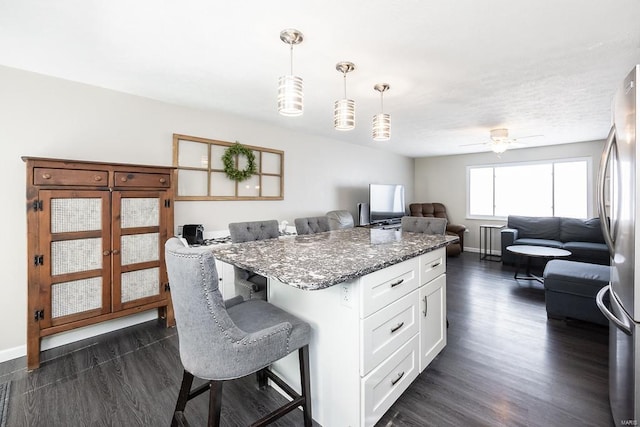 kitchen featuring dark stone countertops, a kitchen breakfast bar, open floor plan, white cabinetry, and freestanding refrigerator