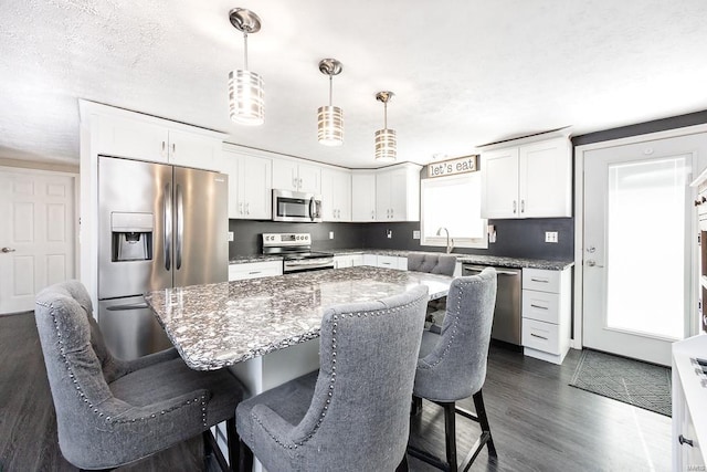 kitchen with dark wood-style floors, a breakfast bar, appliances with stainless steel finishes, white cabinetry, and a center island