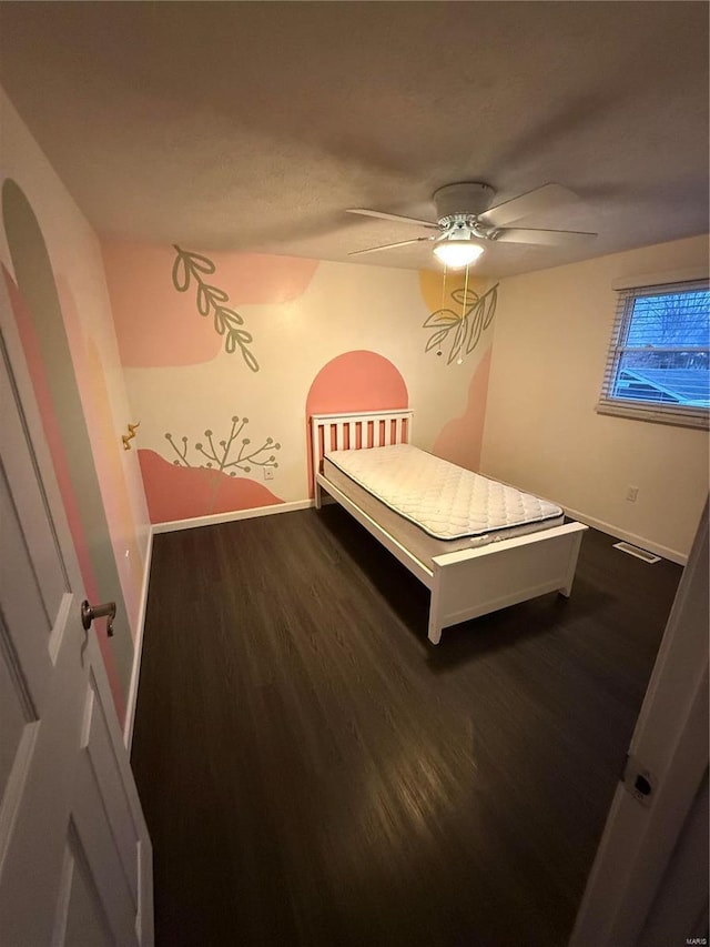 unfurnished bedroom with visible vents, dark wood-type flooring, a ceiling fan, arched walkways, and baseboards