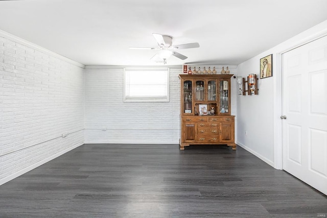 interior space featuring brick wall, baseboards, dark wood-type flooring, and a ceiling fan