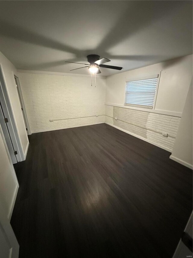 unfurnished bedroom with dark wood finished floors, ceiling fan, brick wall, and wainscoting