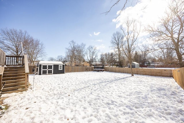 snowy yard with stairway, an outbuilding, a fenced backyard, and a shed