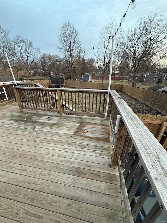 deck with a fenced backyard and a trampoline