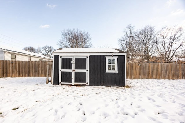 snow covered structure featuring a storage shed, a fenced backyard, and an outdoor structure