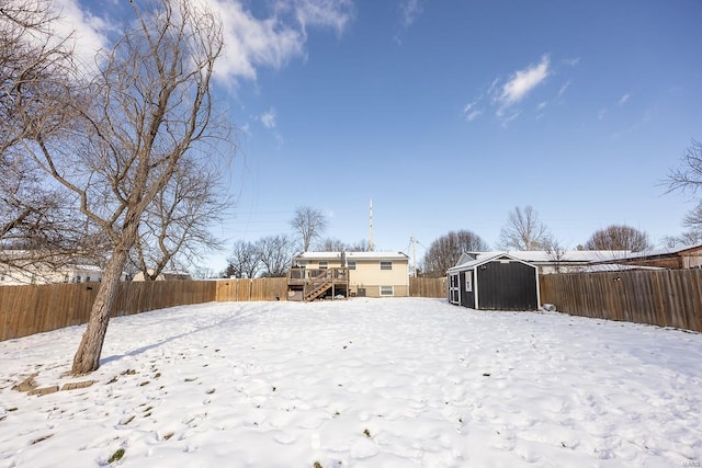 snowy yard featuring a deck, an outbuilding, a fenced backyard, and a storage shed