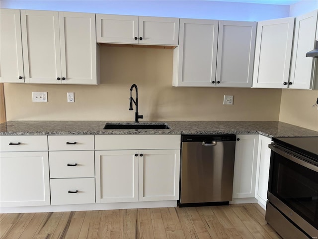 kitchen featuring sink, dark stone countertops, light wood-type flooring, white cabinetry, and stainless steel appliances