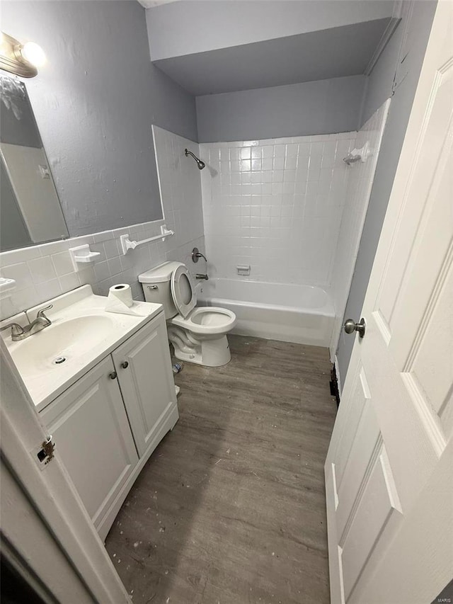 full bathroom with tiled shower / bath combo, wood-type flooring, toilet, vanity, and tile walls