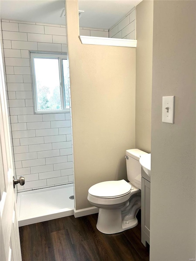 bathroom featuring a tile shower, vanity, wood-type flooring, and toilet