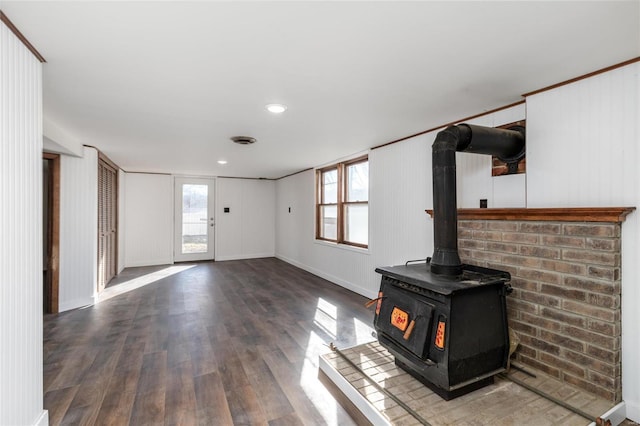 unfurnished living room with hardwood / wood-style floors, wooden walls, a wood stove, and ornamental molding