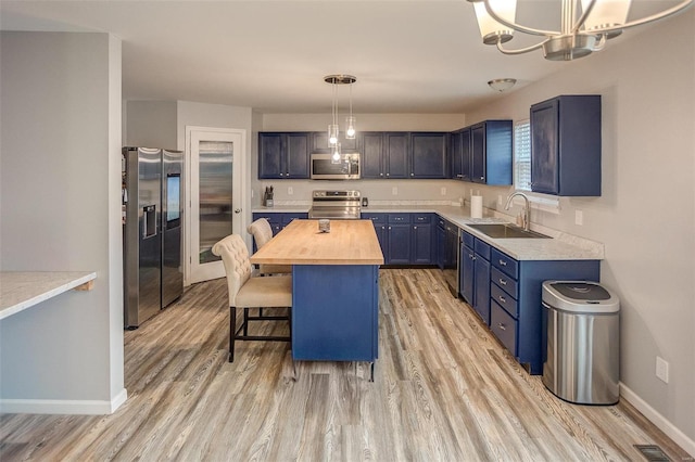 kitchen with a center island, sink, butcher block countertops, decorative light fixtures, and stainless steel appliances