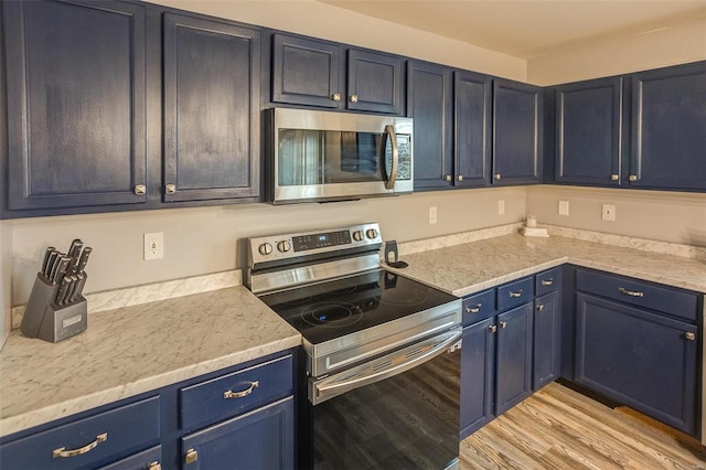 kitchen featuring blue cabinetry, light stone counters, stainless steel appliances, and light hardwood / wood-style floors