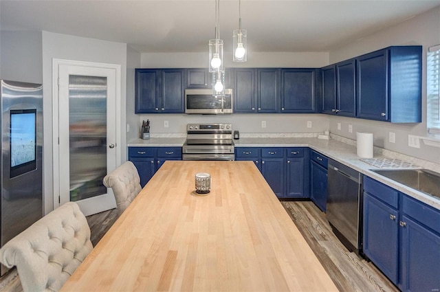 kitchen with blue cabinetry, butcher block counters, decorative light fixtures, appliances with stainless steel finishes, and light wood-type flooring