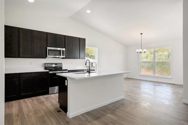 kitchen with a kitchen island with sink, sink, light wood-type flooring, decorative light fixtures, and stainless steel appliances